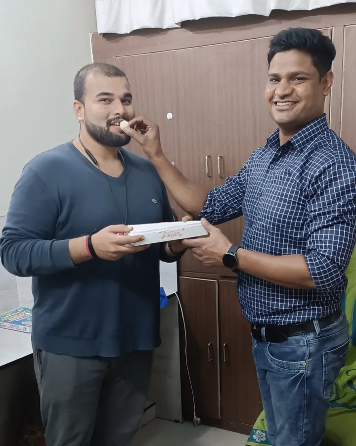 Abhishek Kumar holding a box of sweets and being fed one at the institute, after his IBPS result