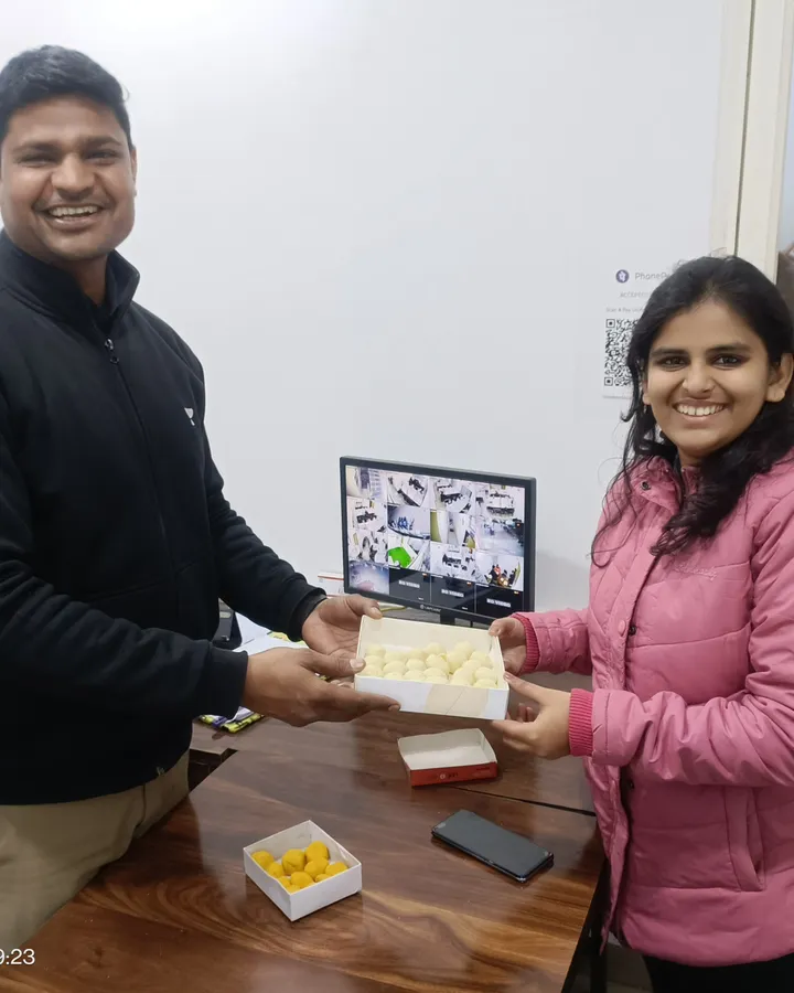 Bhavika Sharma being handed a box of sweets across a desk at the centre after qualifying as a CA