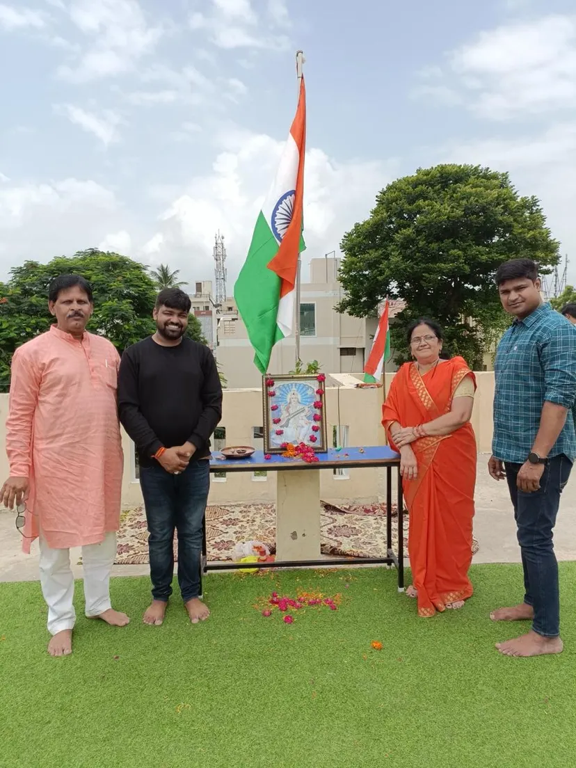 Flag hoisting on the terrace: the Indian tricolour flying beside a garlanded portrait of Saraswati, with four people standing either side