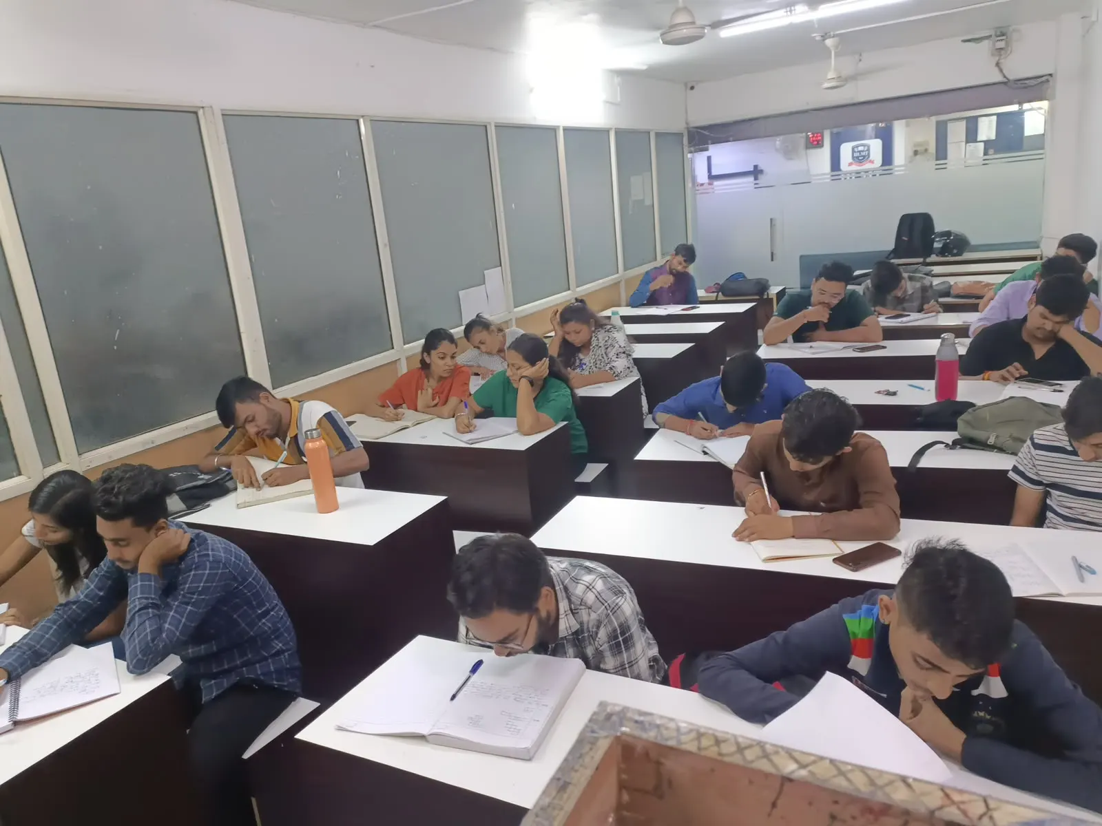 Students writing at their desks in the study hall, seen down the length of the room past the window wall