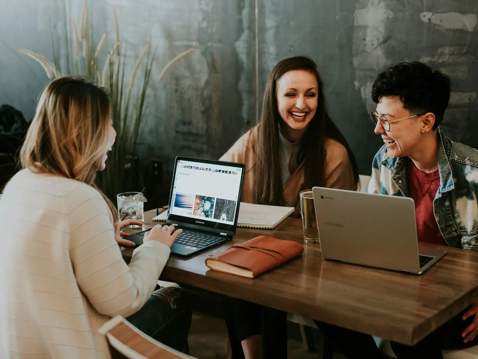 Three students working together at a table with laptops and notes