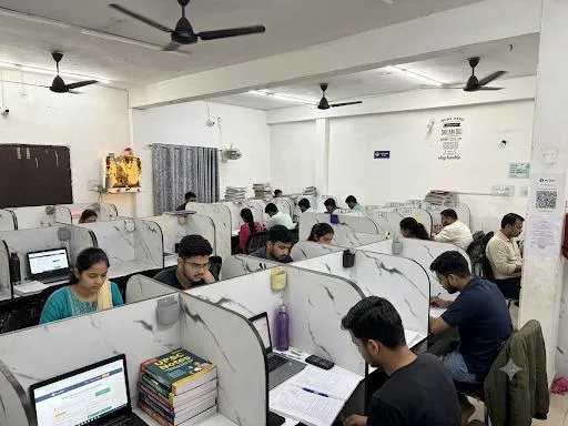 The study hall in use — rows of individual marble-topped cabins with partitions, students working at laptops and books under ceiling fans